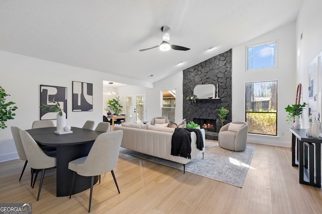 living room with light wood-type flooring, a stone fireplace, a wealth of natural light, and lofted ceiling