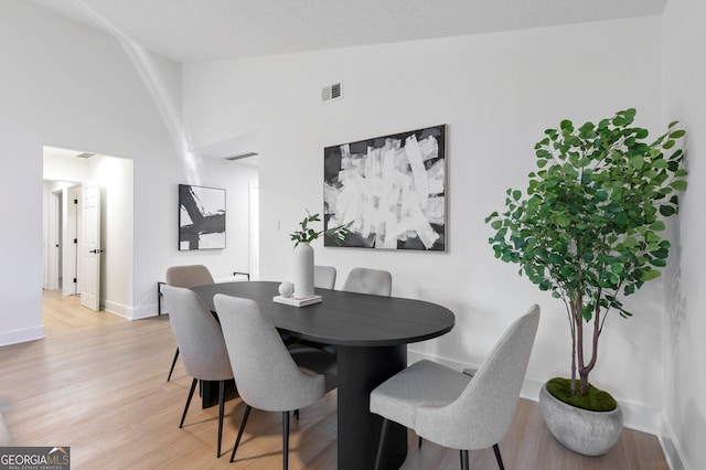 dining space featuring light wood-type flooring and high vaulted ceiling