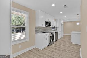 kitchen with light hardwood / wood-style floors, white cabinetry, decorative backsplash, and appliances with stainless steel finishes