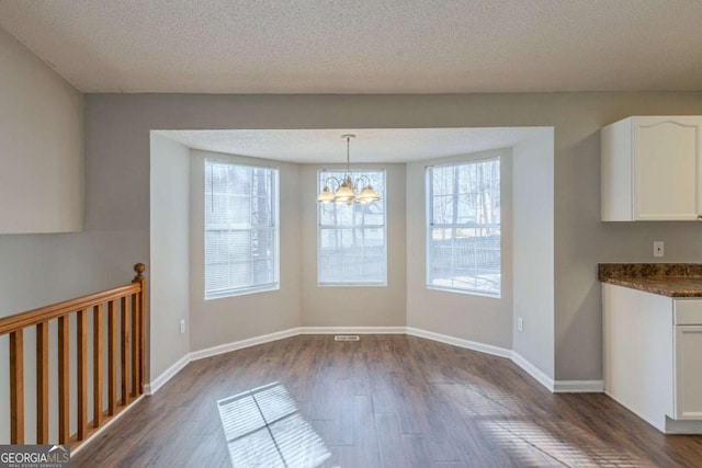 unfurnished dining area featuring a textured ceiling, a chandelier, and dark hardwood / wood-style floors