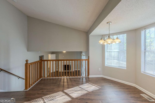 spare room featuring vaulted ceiling, an inviting chandelier, dark wood-type flooring, and a textured ceiling