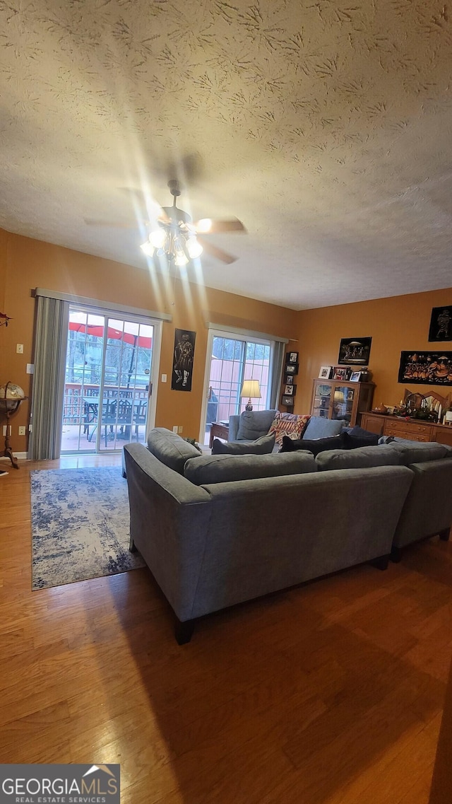 living room featuring dark wood-type flooring, a textured ceiling, and ceiling fan