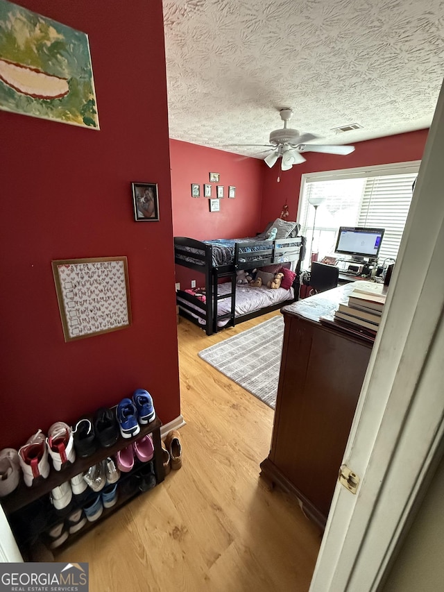 bedroom with hardwood / wood-style flooring, ceiling fan, and a textured ceiling