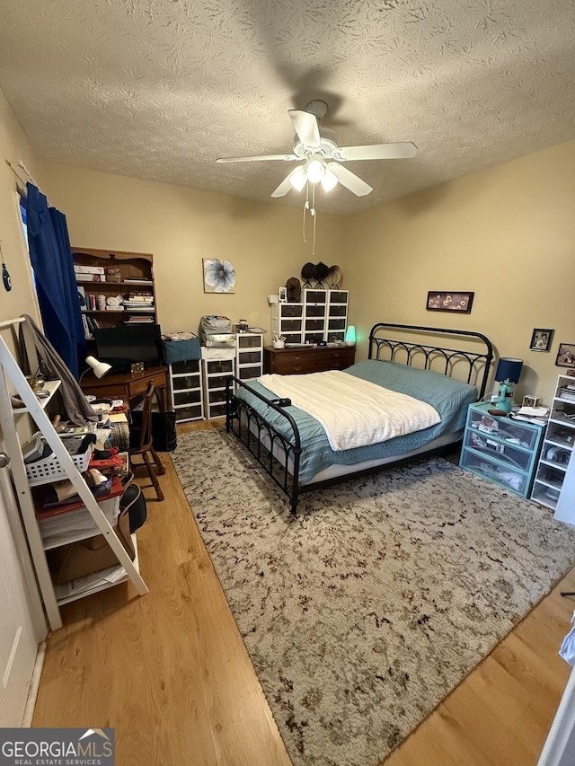 bedroom with ceiling fan, a textured ceiling, and hardwood / wood-style flooring