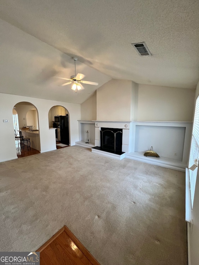 unfurnished living room featuring ceiling fan, lofted ceiling, carpet, and a textured ceiling