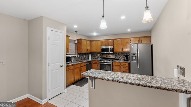 kitchen with decorative light fixtures, appliances with stainless steel finishes, kitchen peninsula, stone counters, and decorative backsplash