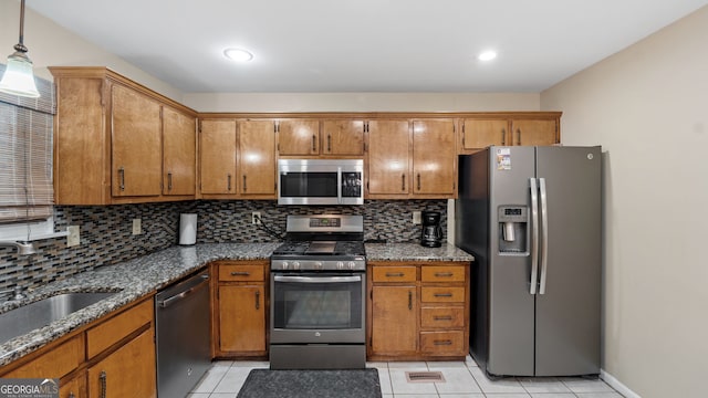 kitchen featuring sink, tasteful backsplash, decorative light fixtures, dark stone countertops, and appliances with stainless steel finishes