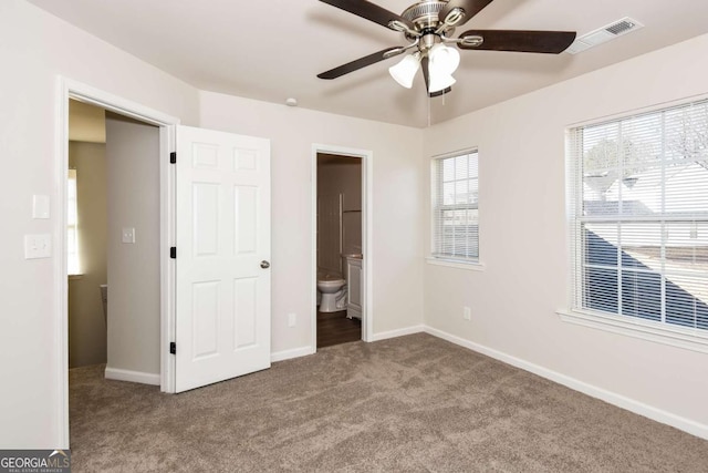 unfurnished bedroom featuring ceiling fan, multiple windows, connected bathroom, and light carpet