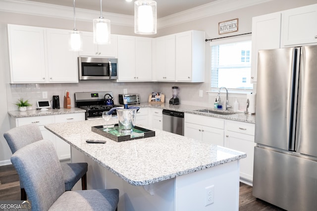 kitchen featuring appliances with stainless steel finishes, white cabinets, hanging light fixtures, a center island, and crown molding