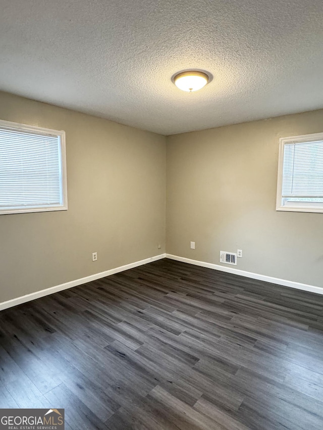 empty room with dark hardwood / wood-style floors and a textured ceiling