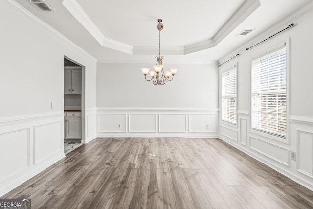 unfurnished dining area featuring wood-type flooring, ornamental molding, a raised ceiling, and a chandelier