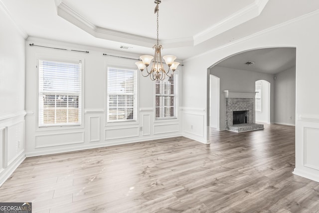 unfurnished dining area featuring a raised ceiling, crown molding, hardwood / wood-style flooring, and a chandelier