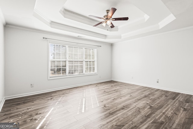 empty room featuring a raised ceiling, ornamental molding, hardwood / wood-style floors, and ceiling fan