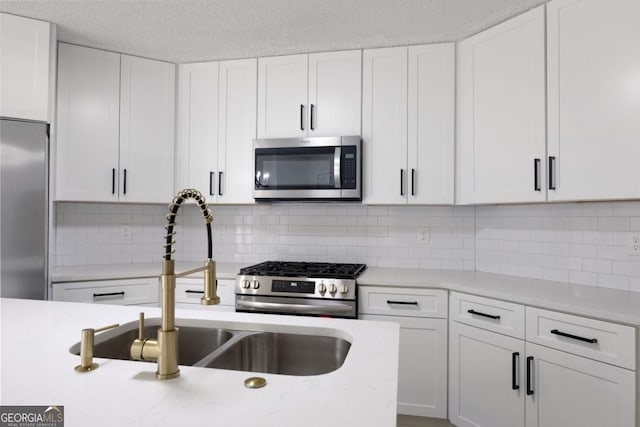 kitchen featuring appliances with stainless steel finishes, sink, white cabinetry, a textured ceiling, and decorative backsplash