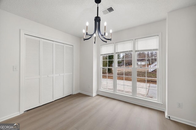 unfurnished dining area with a textured ceiling, a chandelier, and light wood-type flooring