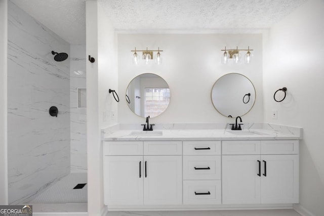 bathroom featuring a textured ceiling, tiled shower, and vanity