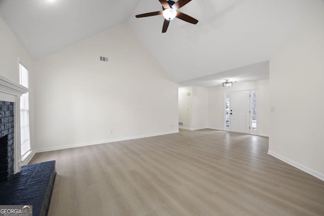 unfurnished living room with ceiling fan, high vaulted ceiling, a brick fireplace, and light hardwood / wood-style floors