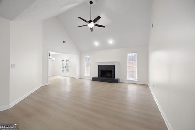 unfurnished living room featuring a fireplace, light hardwood / wood-style flooring, high vaulted ceiling, and ceiling fan