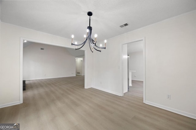 unfurnished dining area with hardwood / wood-style floors, crown molding, a textured ceiling, and a notable chandelier