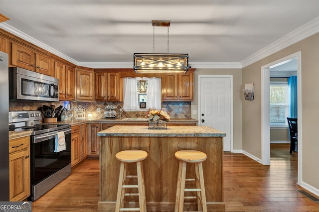 kitchen featuring crown molding, appliances with stainless steel finishes, hardwood / wood-style floors, a center island, and decorative backsplash