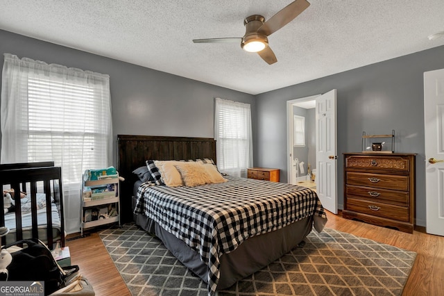 bedroom with ceiling fan, ensuite bathroom, light hardwood / wood-style floors, and a textured ceiling