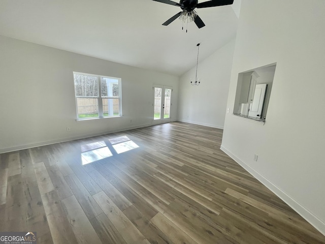 unfurnished living room with french doors, wood finished floors, high vaulted ceiling, baseboards, and ceiling fan with notable chandelier