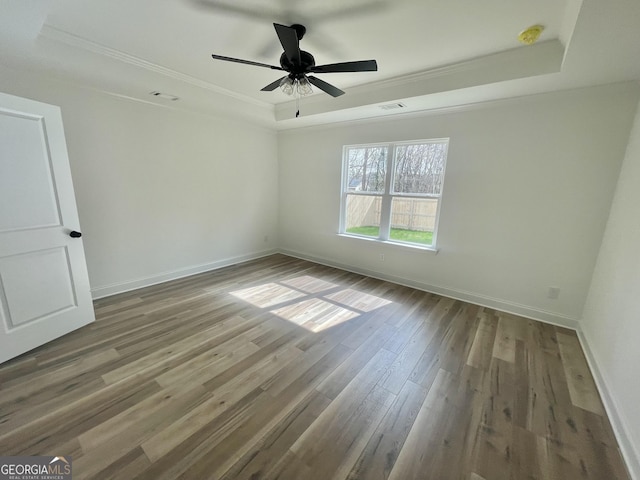 unfurnished bedroom with a tray ceiling, wood finished floors, visible vents, and baseboards