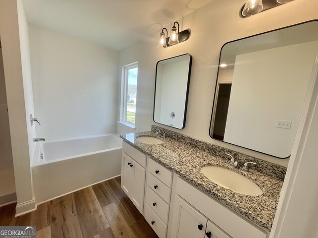 full bathroom featuring a garden tub, double vanity, wood finished floors, and a sink