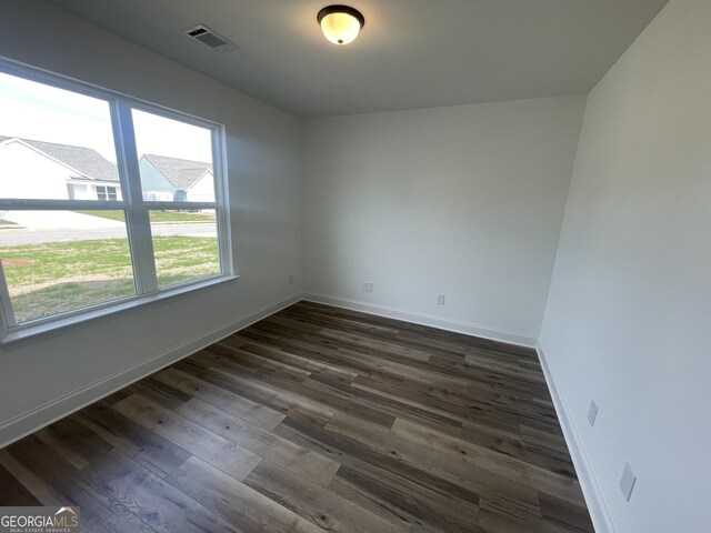 spare room with dark wood finished floors, visible vents, and baseboards