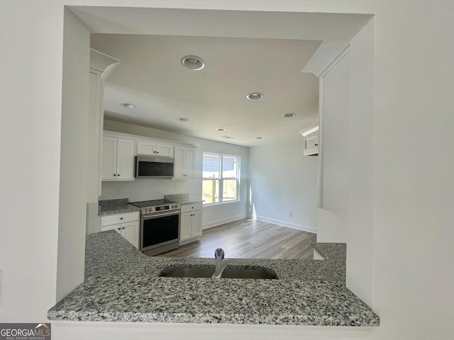 kitchen with appliances with stainless steel finishes, a peninsula, light stone countertops, white cabinetry, and a sink