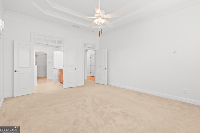 unfurnished bedroom with a spacious closet, crown molding, light carpet, ceiling fan, and a tray ceiling