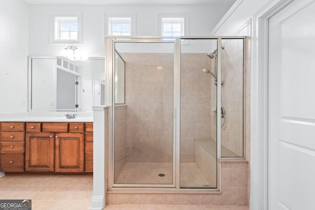 bathroom with vanity, a shower with shower door, a healthy amount of sunlight, and tile patterned floors