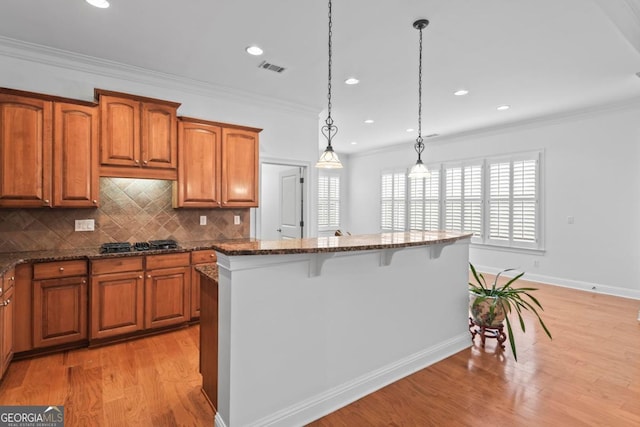 kitchen featuring decorative light fixtures, stainless steel gas stovetop, a kitchen island, and dark stone countertops