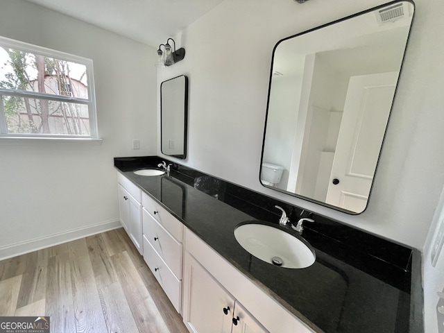 full bath featuring double vanity, toilet, a sink, wood finished floors, and baseboards