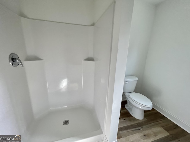 bathroom with a stall shower, wood finished floors, toilet, and baseboards