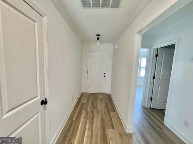 corridor with light wood finished floors, baseboards, visible vents, and crown molding