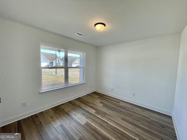 empty room with wood finished floors, visible vents, and baseboards