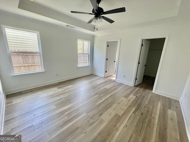 unfurnished bedroom with light wood finished floors, visible vents, baseboards, and a raised ceiling