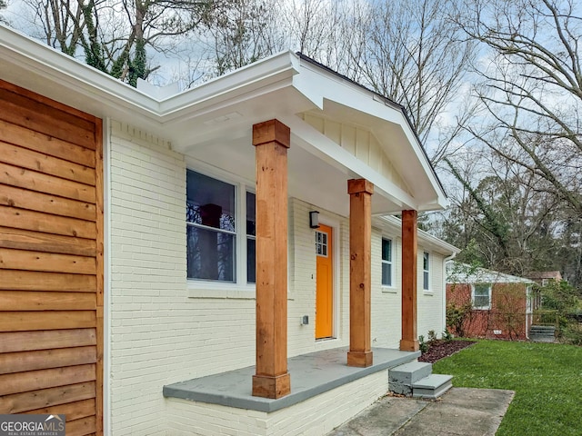 property entrance with a porch, a lawn, and brick siding