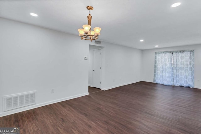 spare room featuring dark wood-type flooring and a chandelier