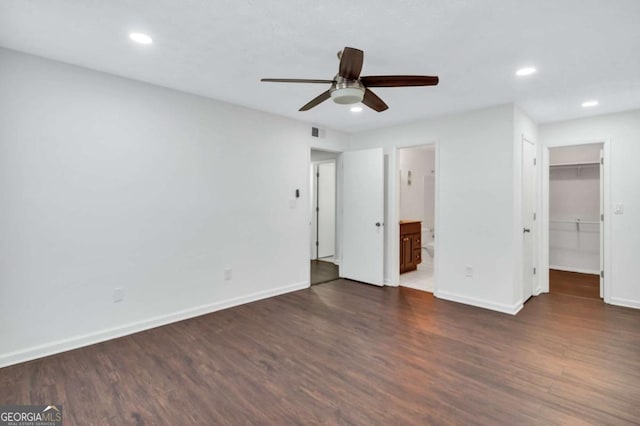 unfurnished bedroom featuring ceiling fan, a spacious closet, dark wood-type flooring, and ensuite bath