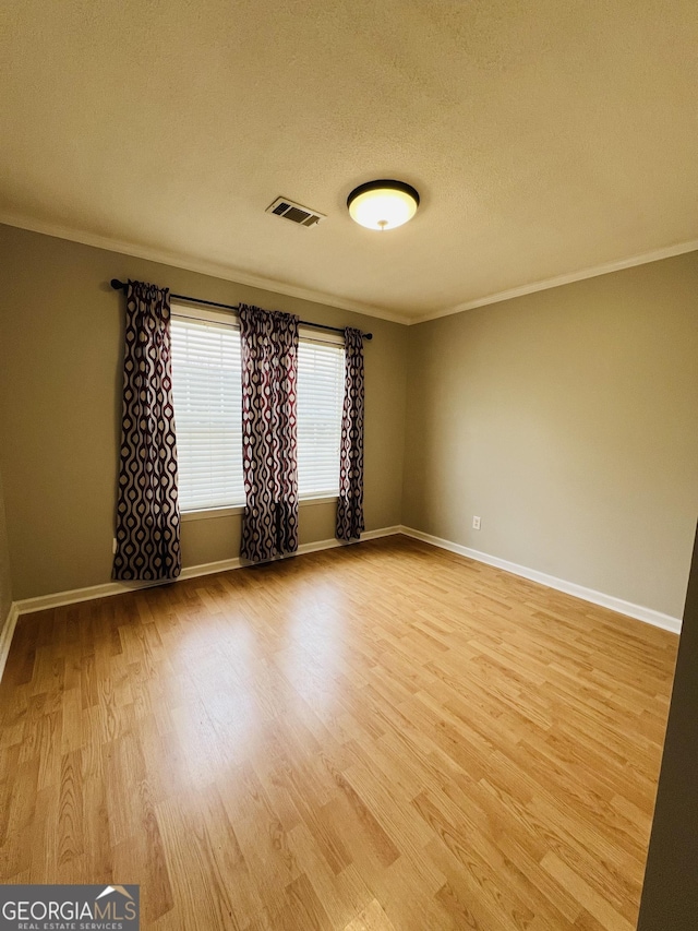 spare room featuring ornamental molding, light hardwood / wood-style floors, and a textured ceiling