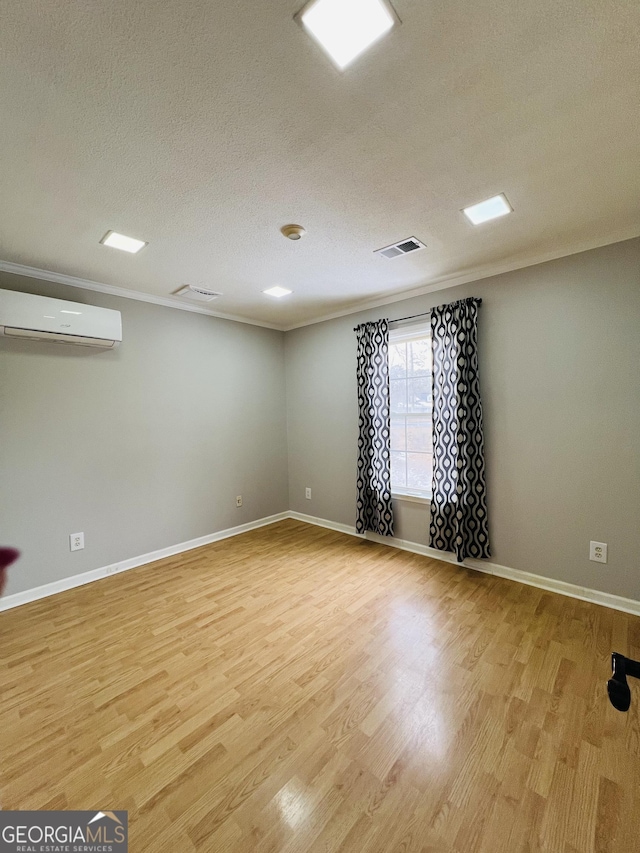 spare room featuring light hardwood / wood-style floors, a textured ceiling, ornamental molding, and a wall unit AC