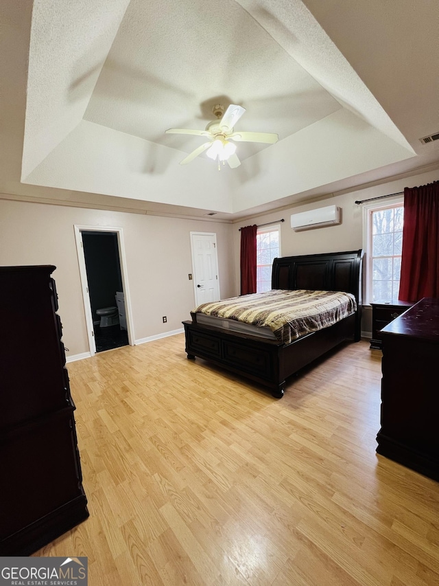 bedroom featuring an AC wall unit, a textured ceiling, a raised ceiling, ceiling fan, and light hardwood / wood-style flooring