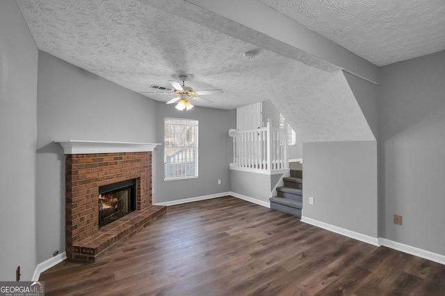 unfurnished living room featuring dark wood-type flooring, a textured ceiling, a fireplace, and ceiling fan