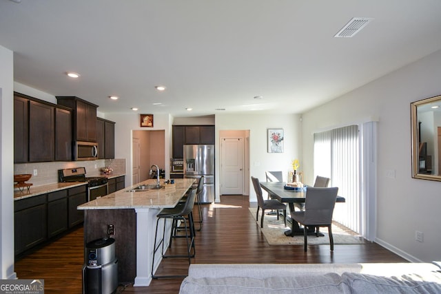 kitchen featuring sink, dark wood-type flooring, appliances with stainless steel finishes, a kitchen island with sink, and light stone countertops