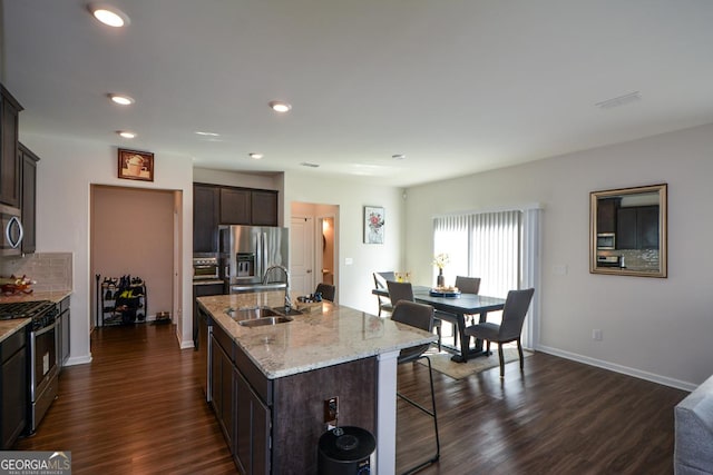 kitchen with sink, dark brown cabinets, appliances with stainless steel finishes, dark hardwood / wood-style floors, and a kitchen island with sink