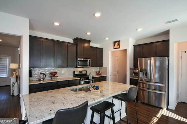 kitchen featuring dark wood-type flooring, appliances with stainless steel finishes, a kitchen island with sink, and backsplash