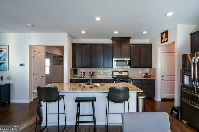 kitchen featuring light stone counters, an island with sink, appliances with stainless steel finishes, and sink