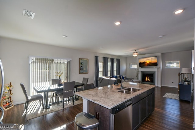 kitchen featuring dishwasher, sink, a kitchen island with sink, light stone counters, and dark wood-type flooring